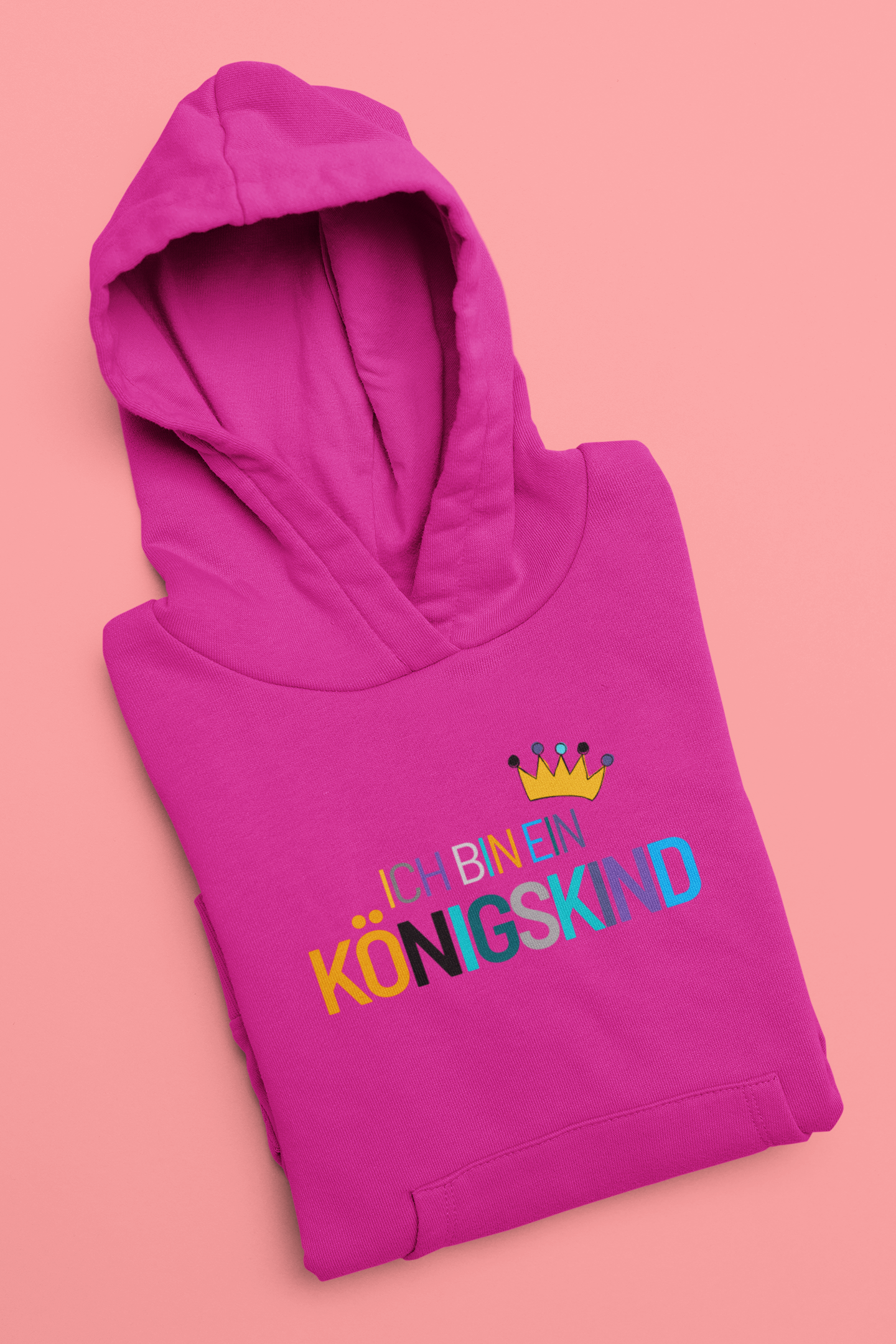 Folded pink hoodie with colorful text and a crown on a pink background