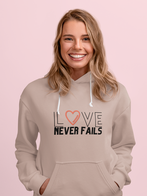 Woman wearing a beige hoodie with 'LOVE NEVER FAILS' text on a pink background