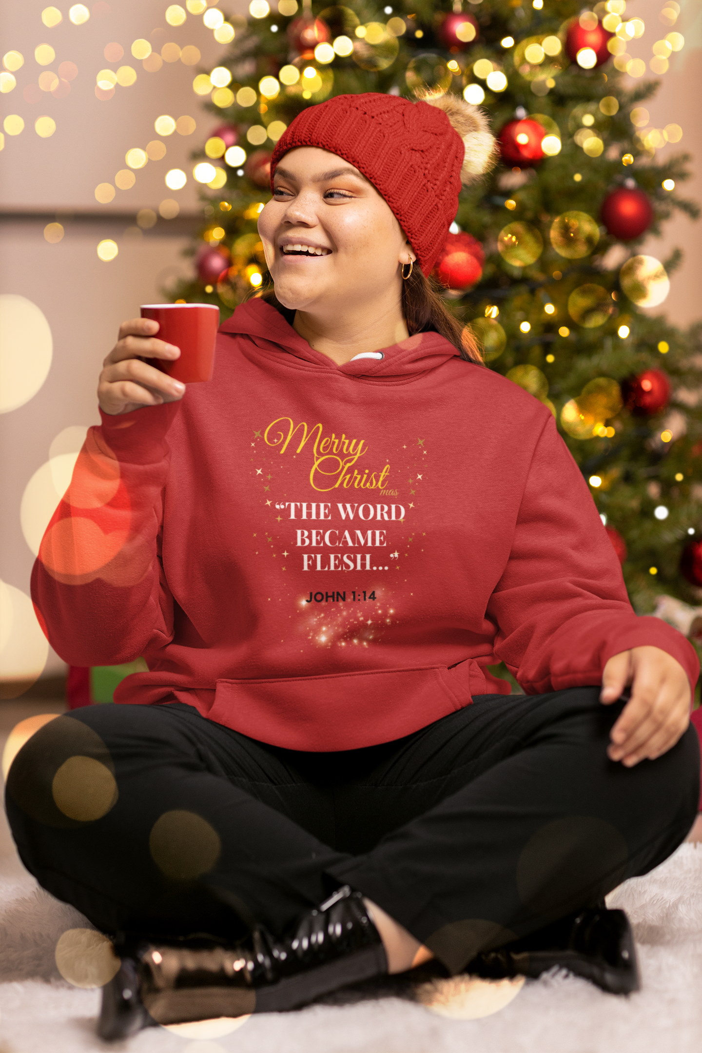 Person wearing a red hoodie with Christmas-themed text, sitting in front of a decorated tree.