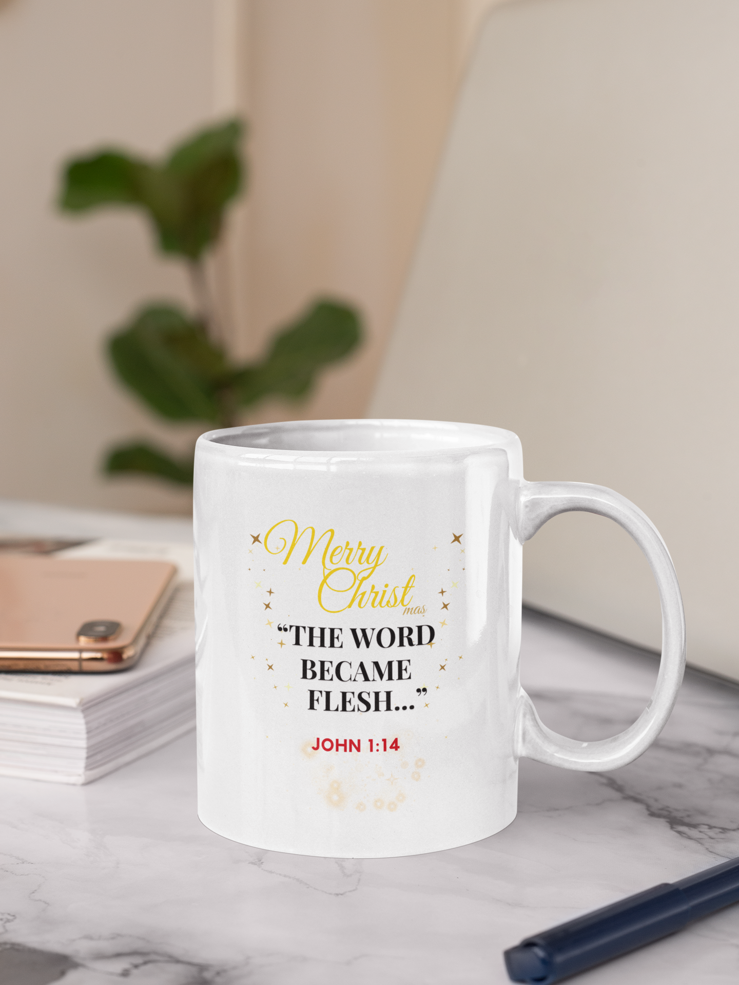 White mug with Christmas text on a marble surface with a plant and notebook in the background