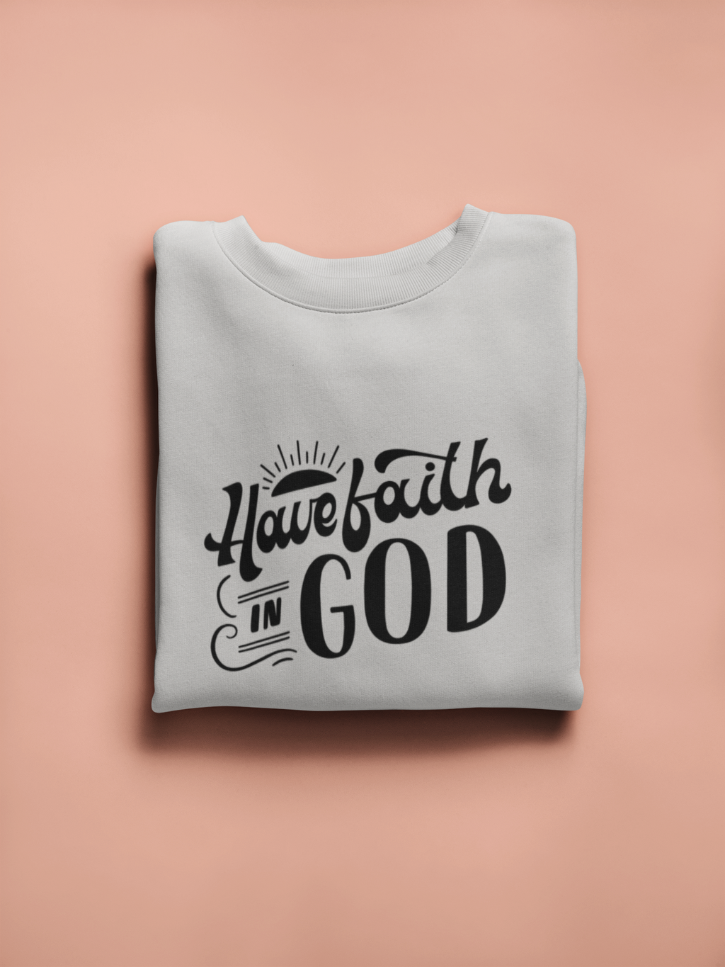 Folded gray sweatshirt with 'Have faith in God' text on a pink background