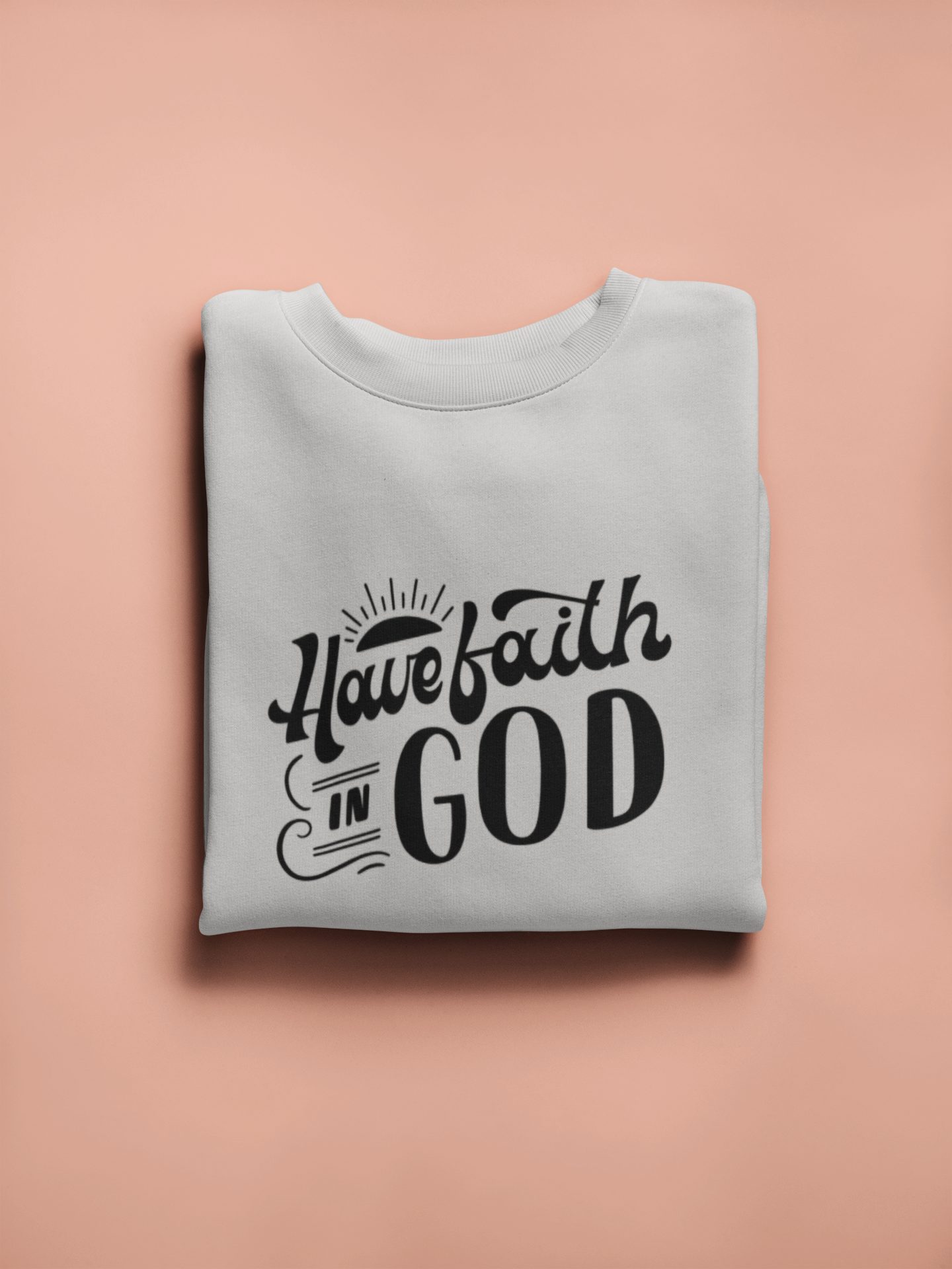 Folded gray sweatshirt with 'Have faith in God' text on a pink background