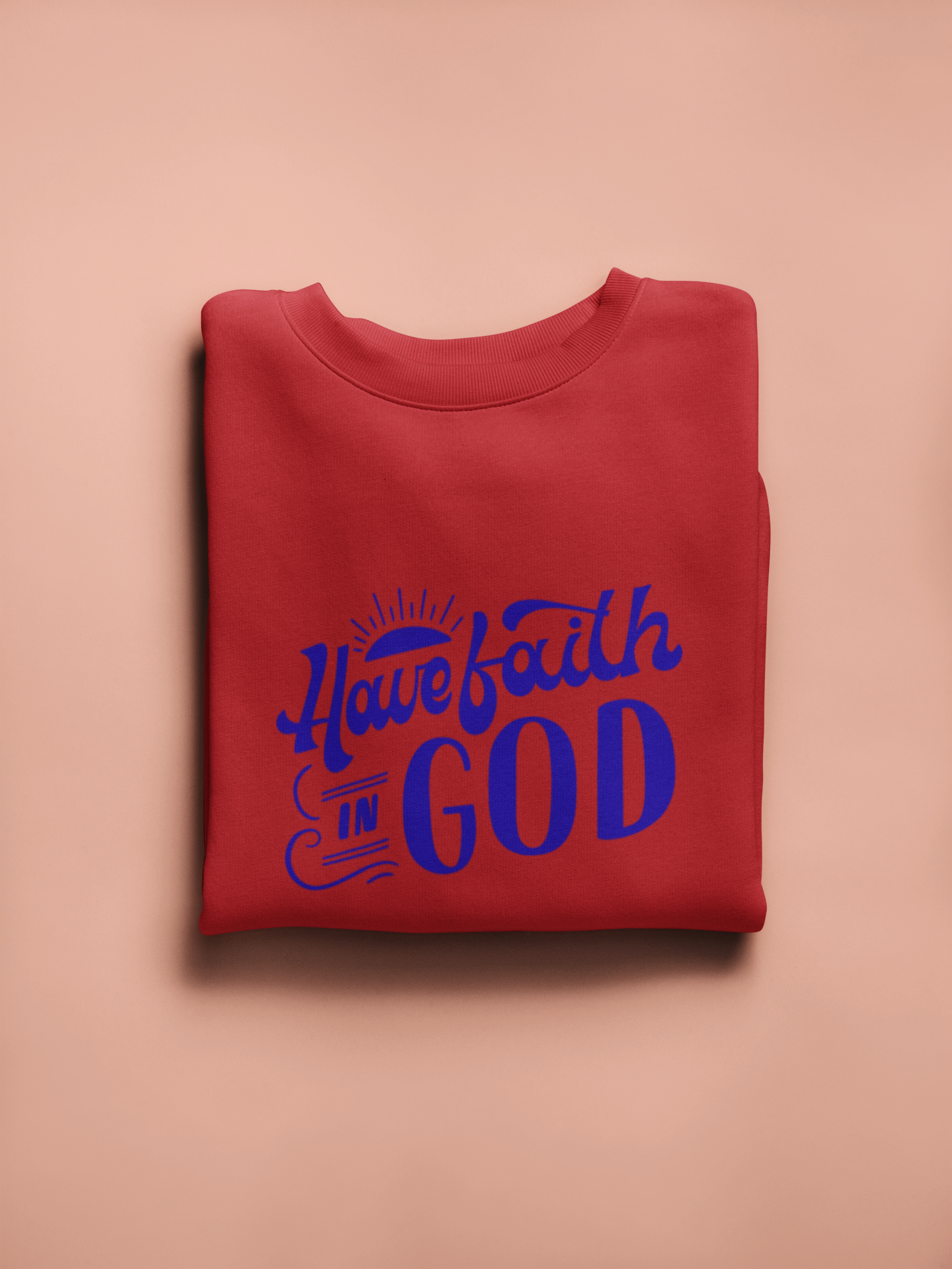 Folded red sweatshirt with blue text 'Have faith in GOD' on a beige background