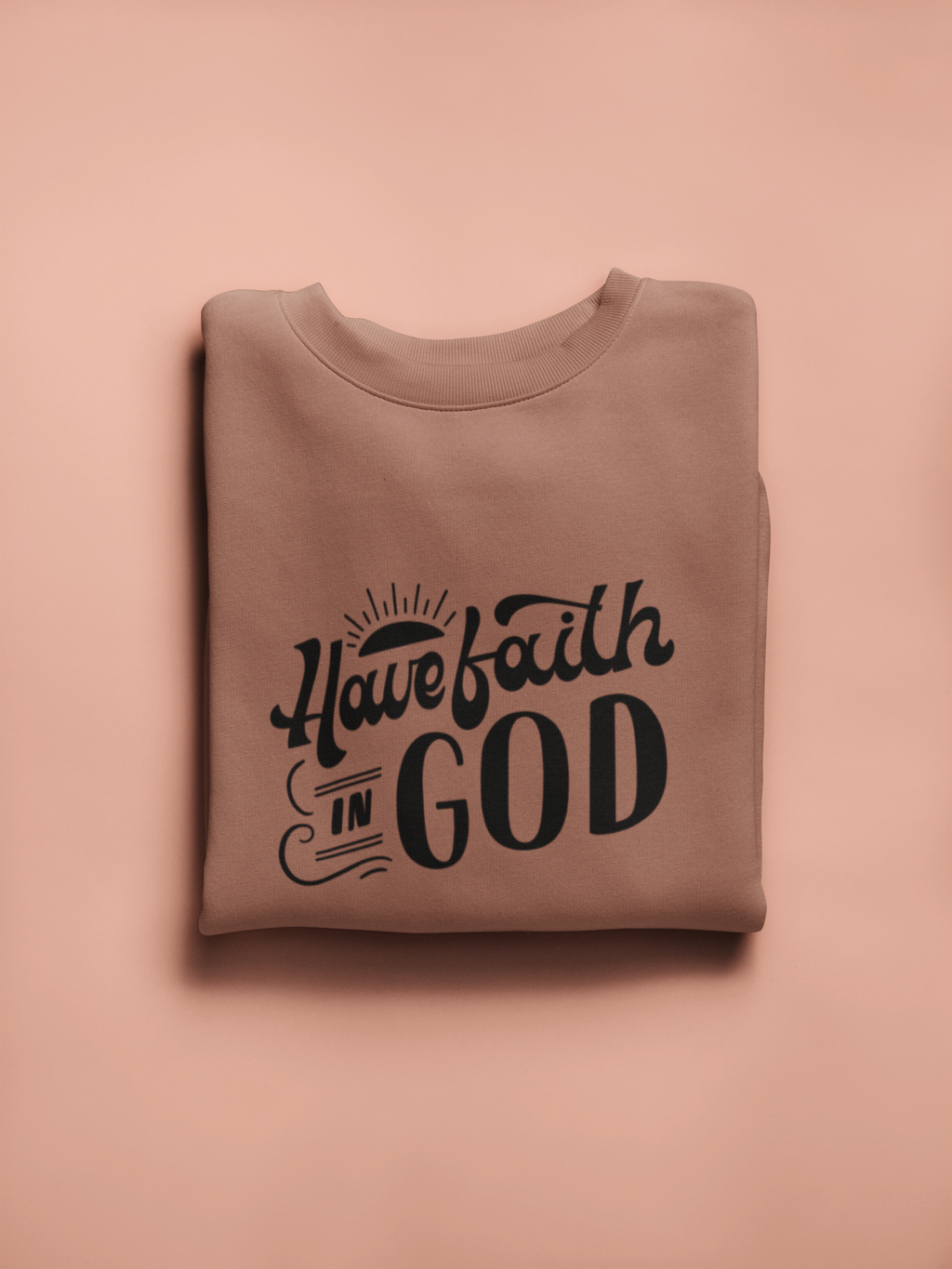 Folded brown sweatshirt with 'Have faith in God' text on a pink background