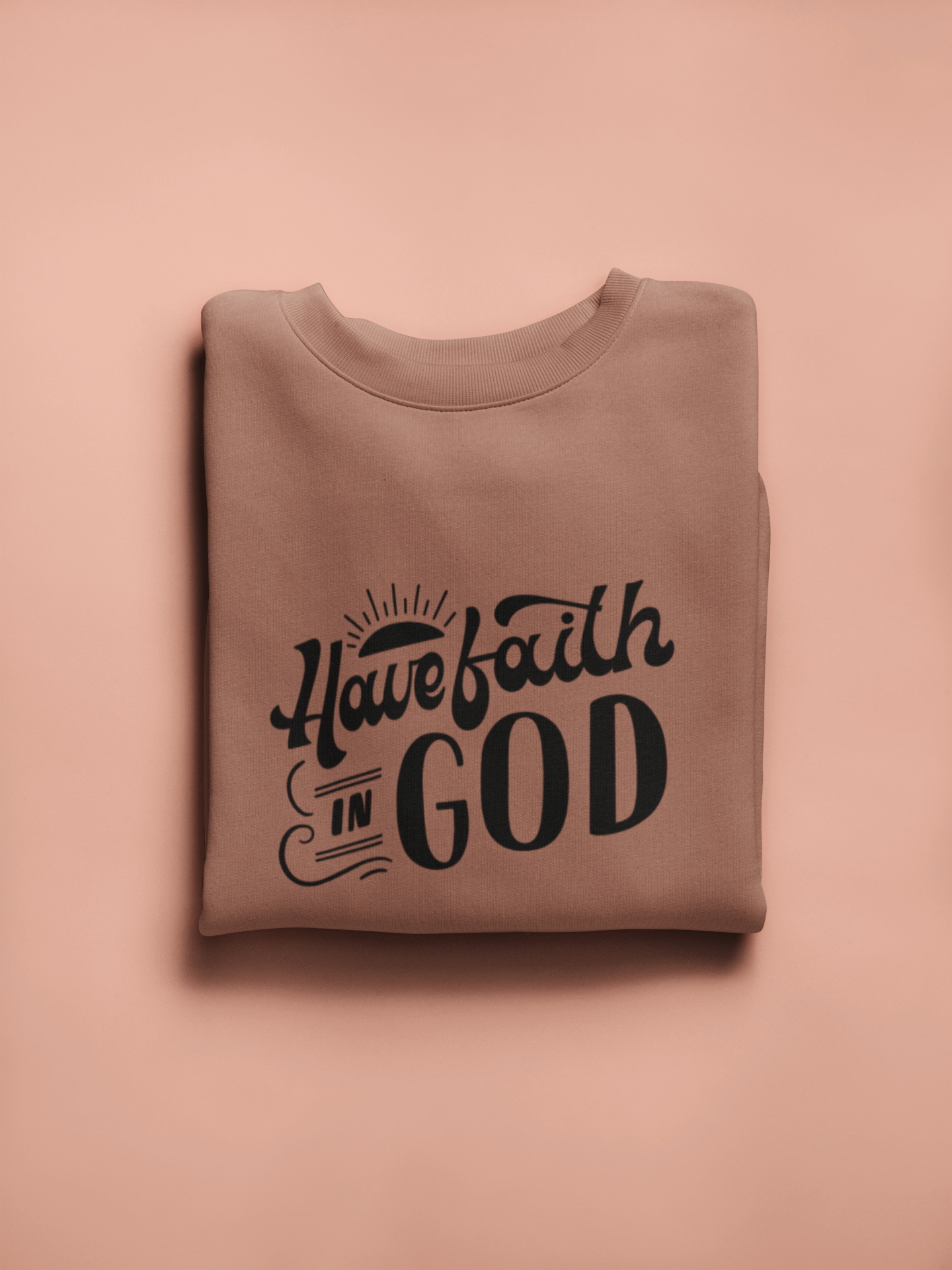 Folded brown sweatshirt with 'Have faith in God' text on a pink background