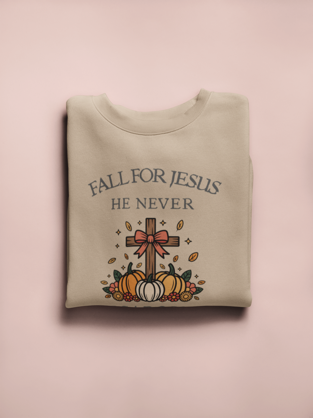 Folded sweatshirt with 'Fall for Jesus He Never' text and cross design on a pink background