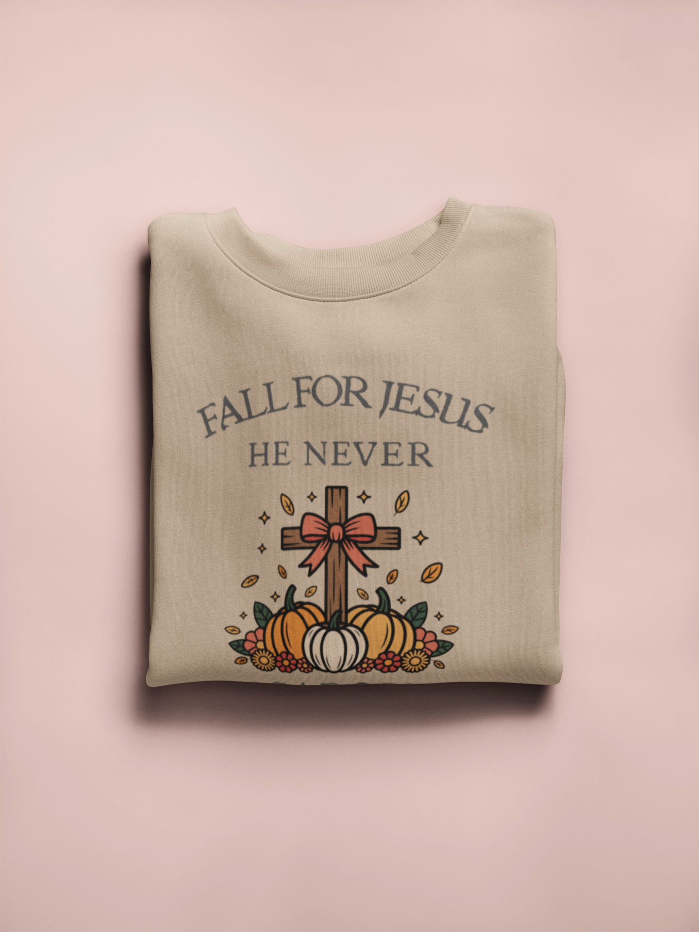 Folded sweatshirt with 'Fall for Jesus He Never' text and cross design on a pink background