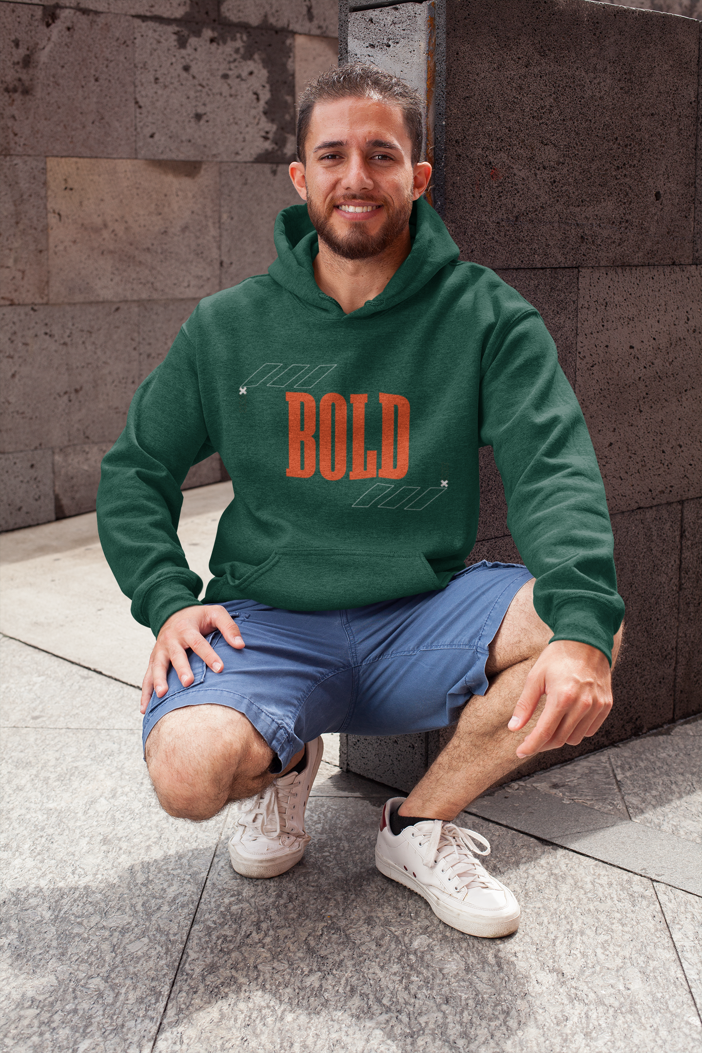 Man wearing a green hoodie with 'BOLD' text, sitting on a stone surface.