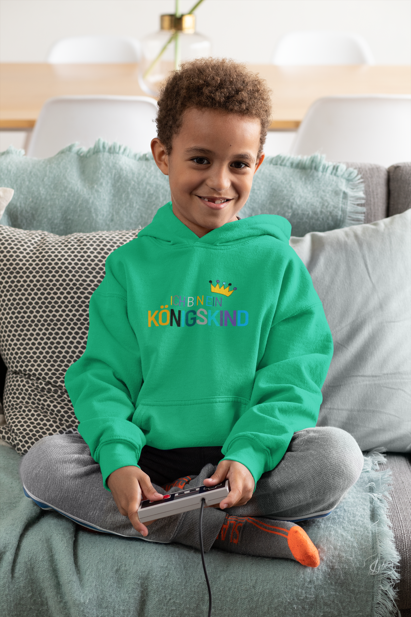 Child wearing a green hoodie with colorful text, sitting on a couch.