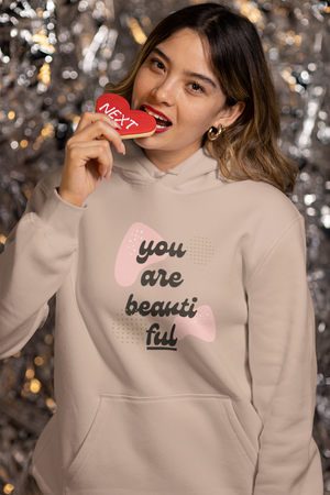 Woman wearing a beige hoodie with text and a heart design, holding a red heart-shaped object.