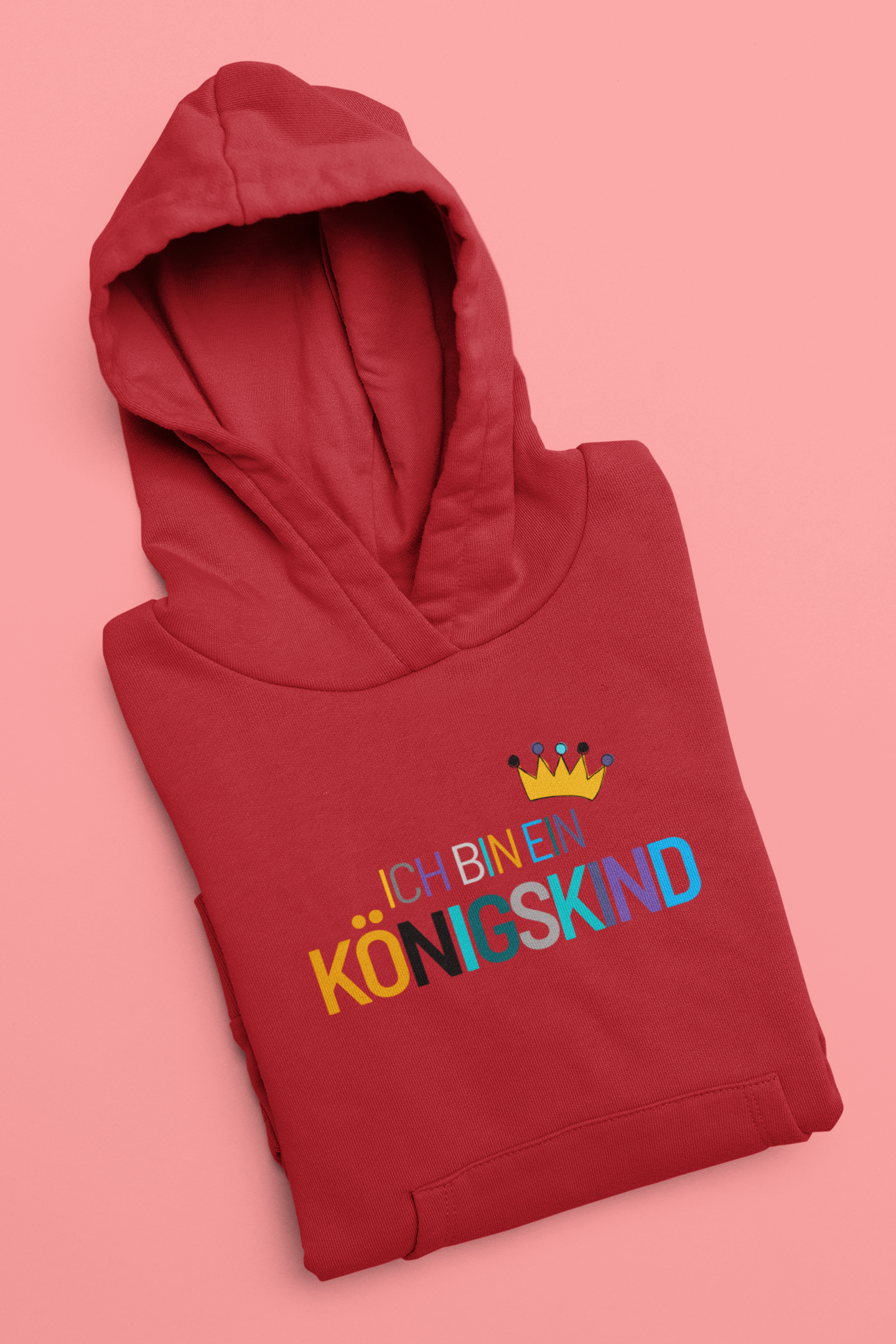 Folded red hoodie with colorful text and crown design on a pink background