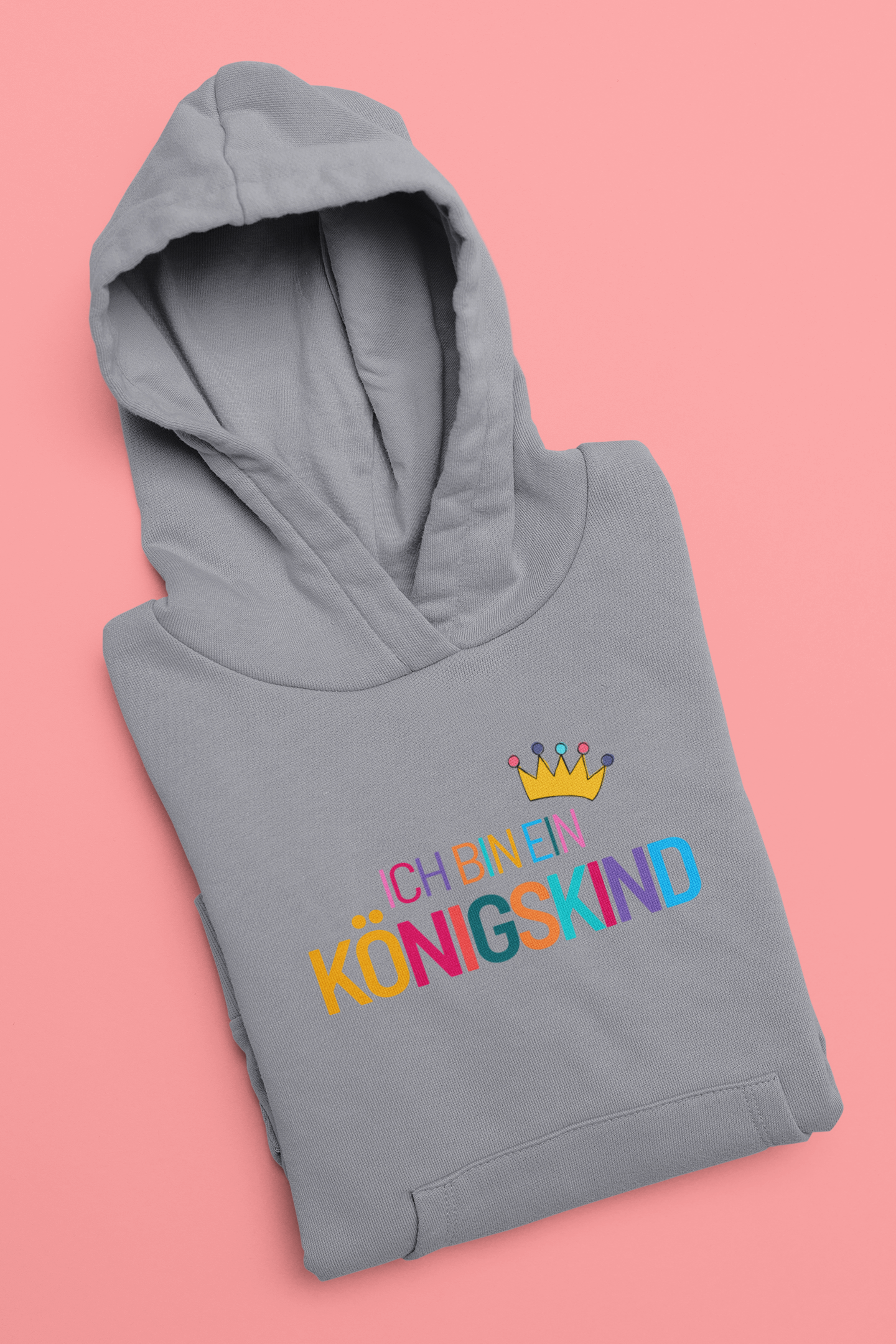 Folded gray hoodie with colorful text and a crown on a pink background