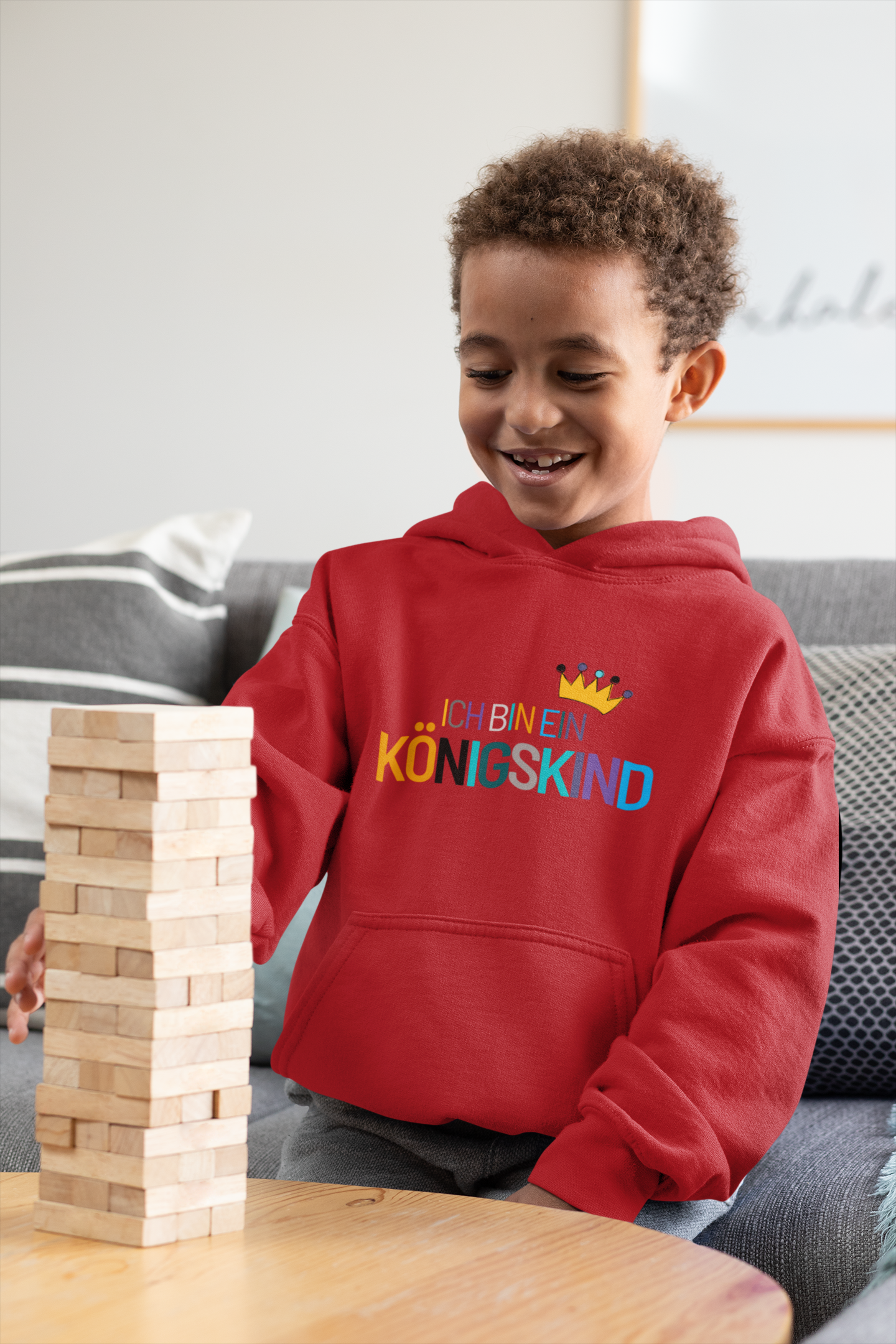 Child playing with wooden blocks on a table, wearing a red hoodie with colorful text.