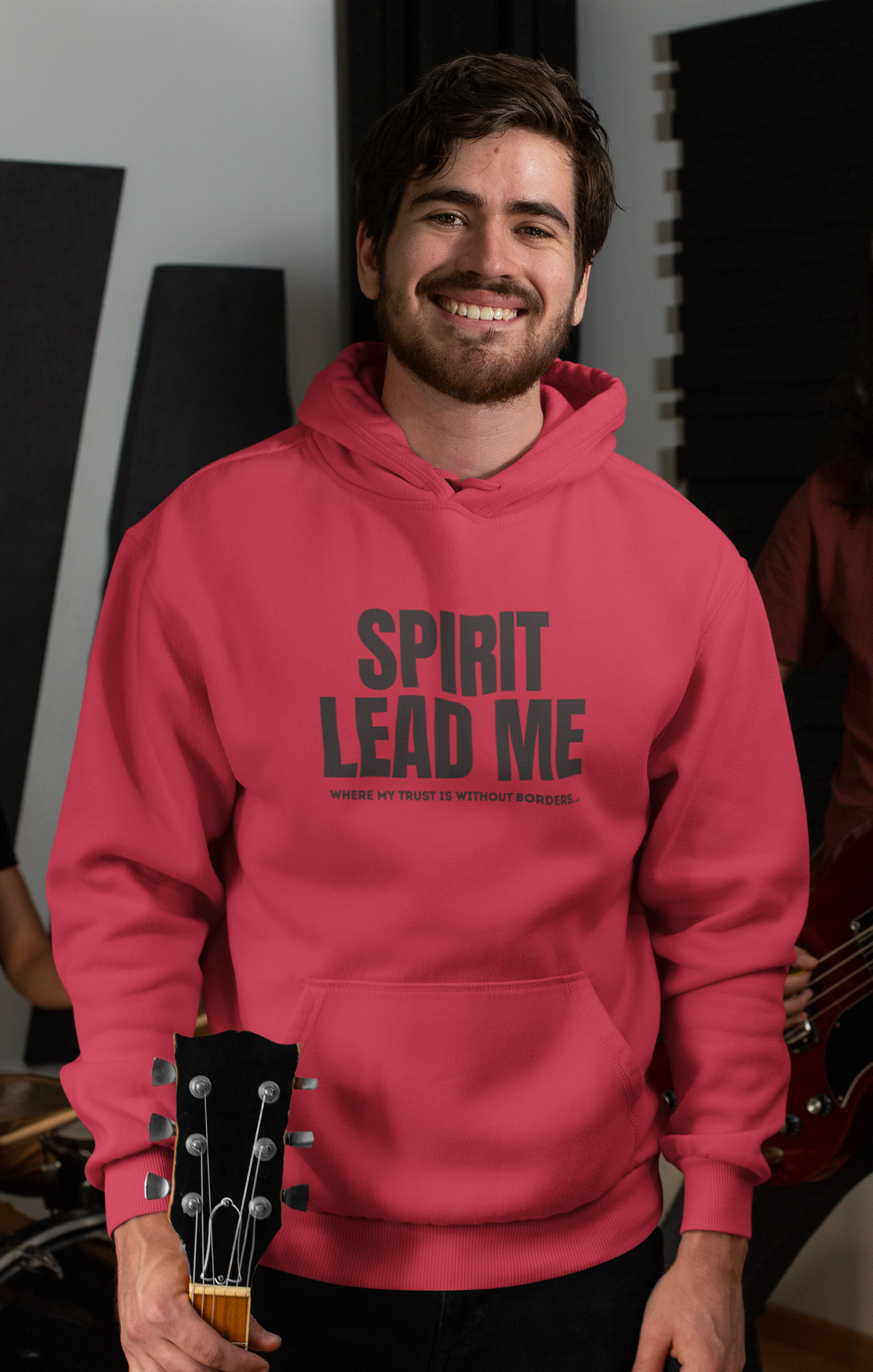 Man wearing a pink hoodie with 'SPIRIT LEAD ME' text, holding a guitar in an indoor setting.