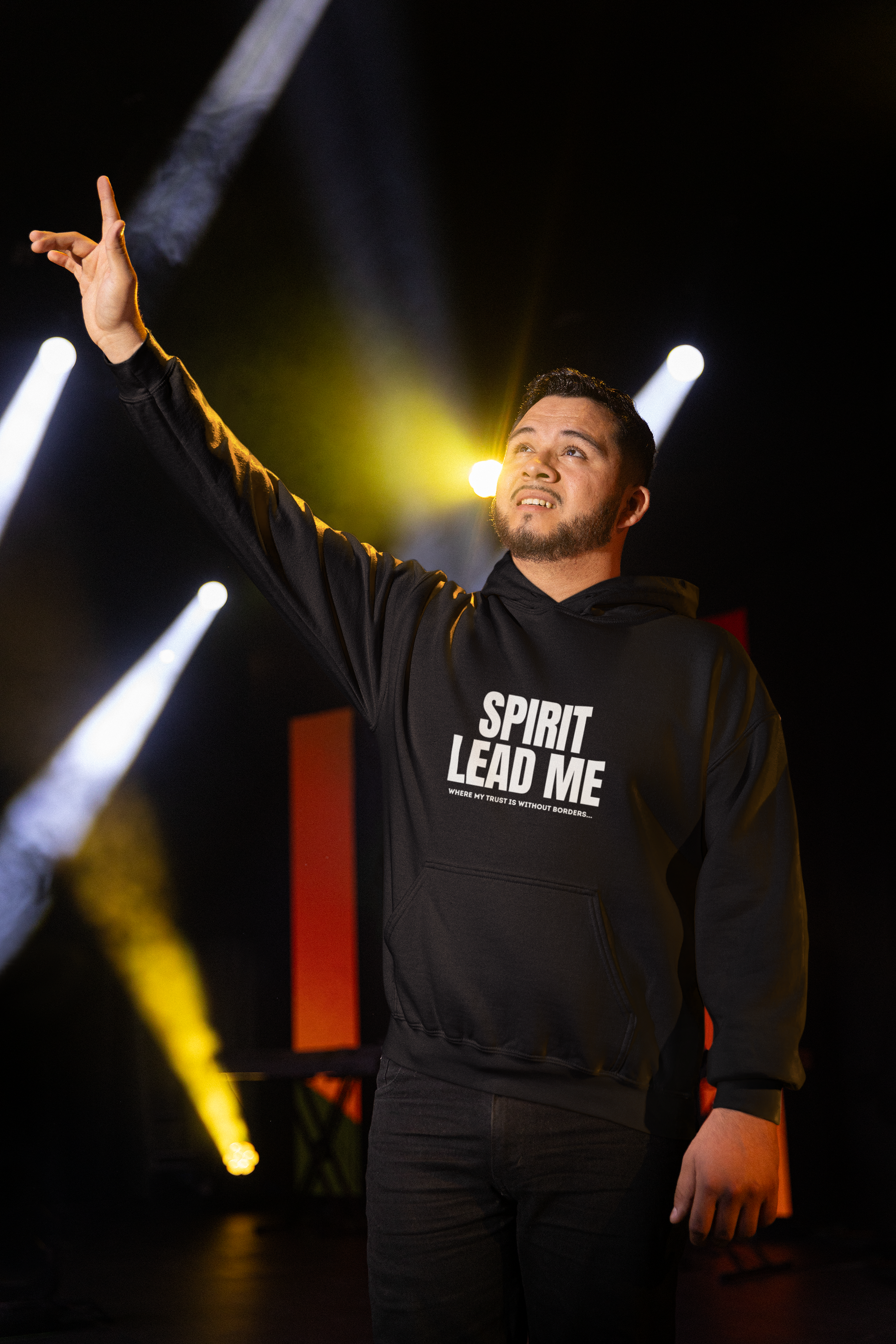 Person wearing a black hoodie with 'SPIRIT LEAD ME' text, standing on a stage with lights in the background.