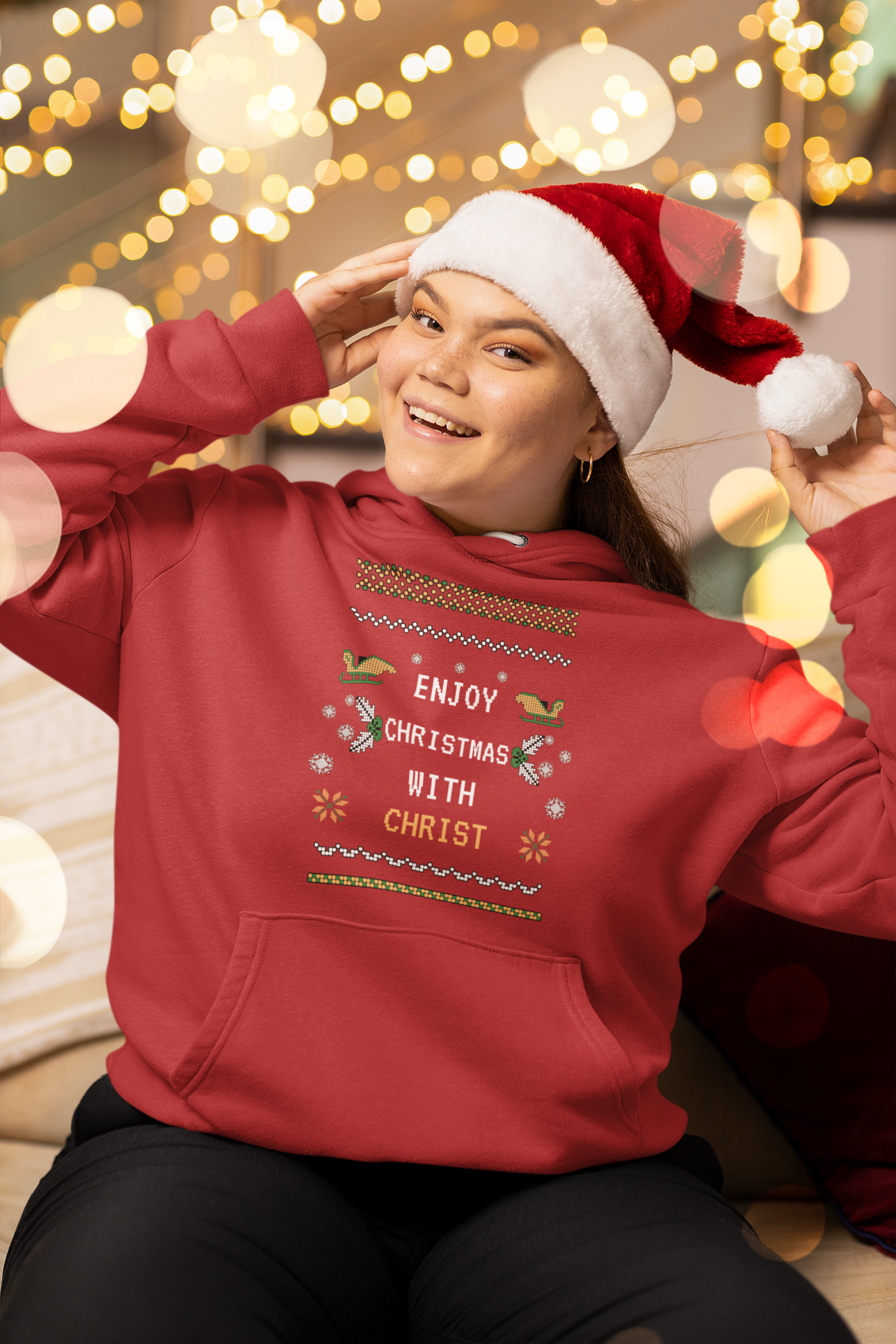 Person wearing a red hoodie with Christmas-themed text and a Santa hat, sitting against a festive background.