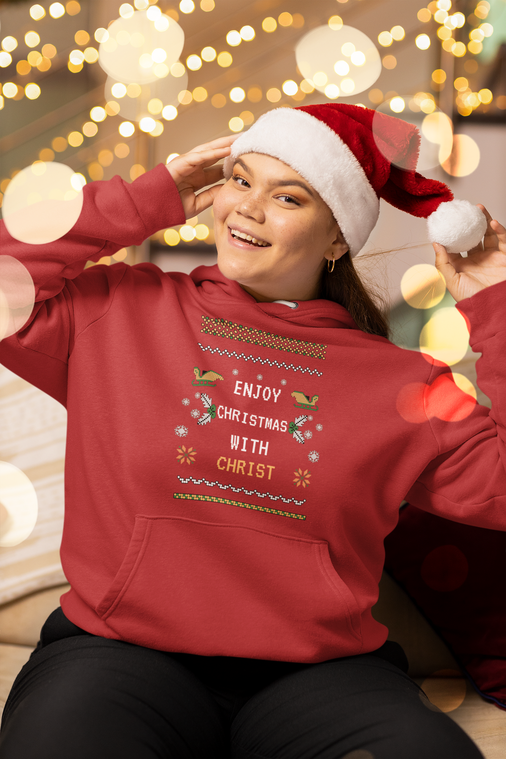Person wearing a red hoodie with Christmas-themed text and a Santa hat, sitting against a festive background.