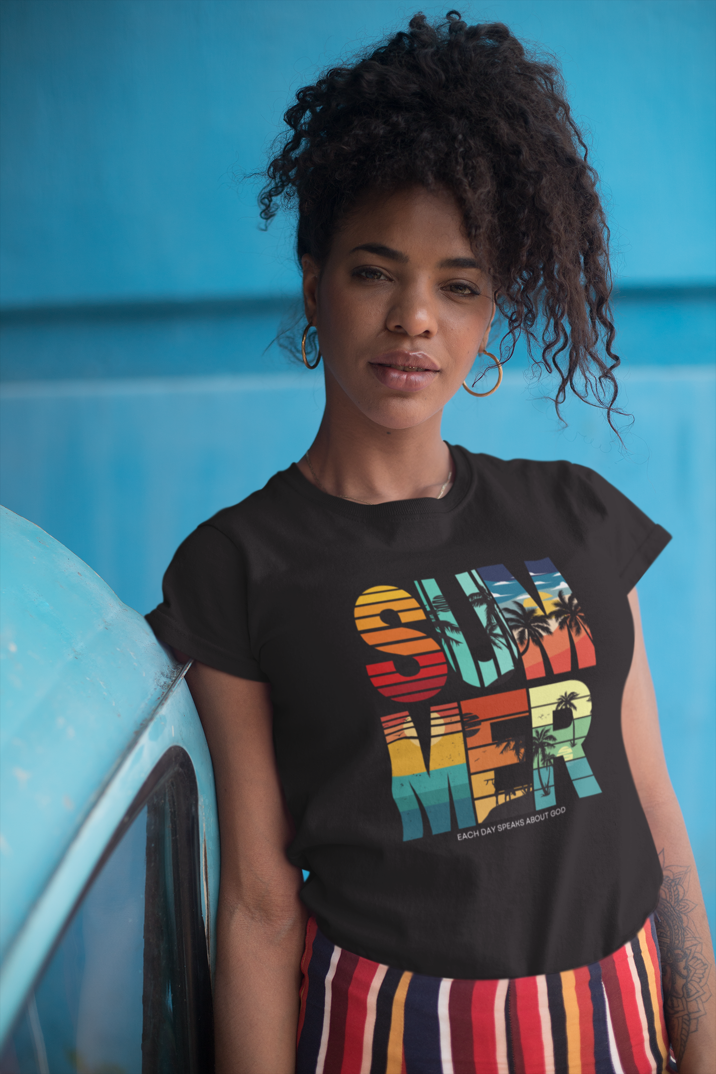 Person wearing a black t-shirt with colorful text design in front of a blue vehicle.