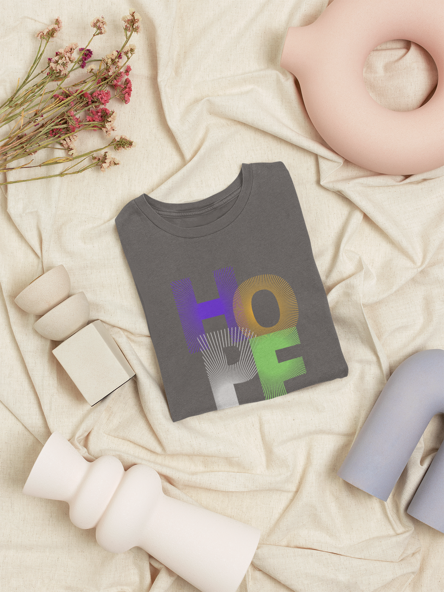 Gray t-shirt with 'HOPE' printed in colorful letters on a beige surface with decorative elements.