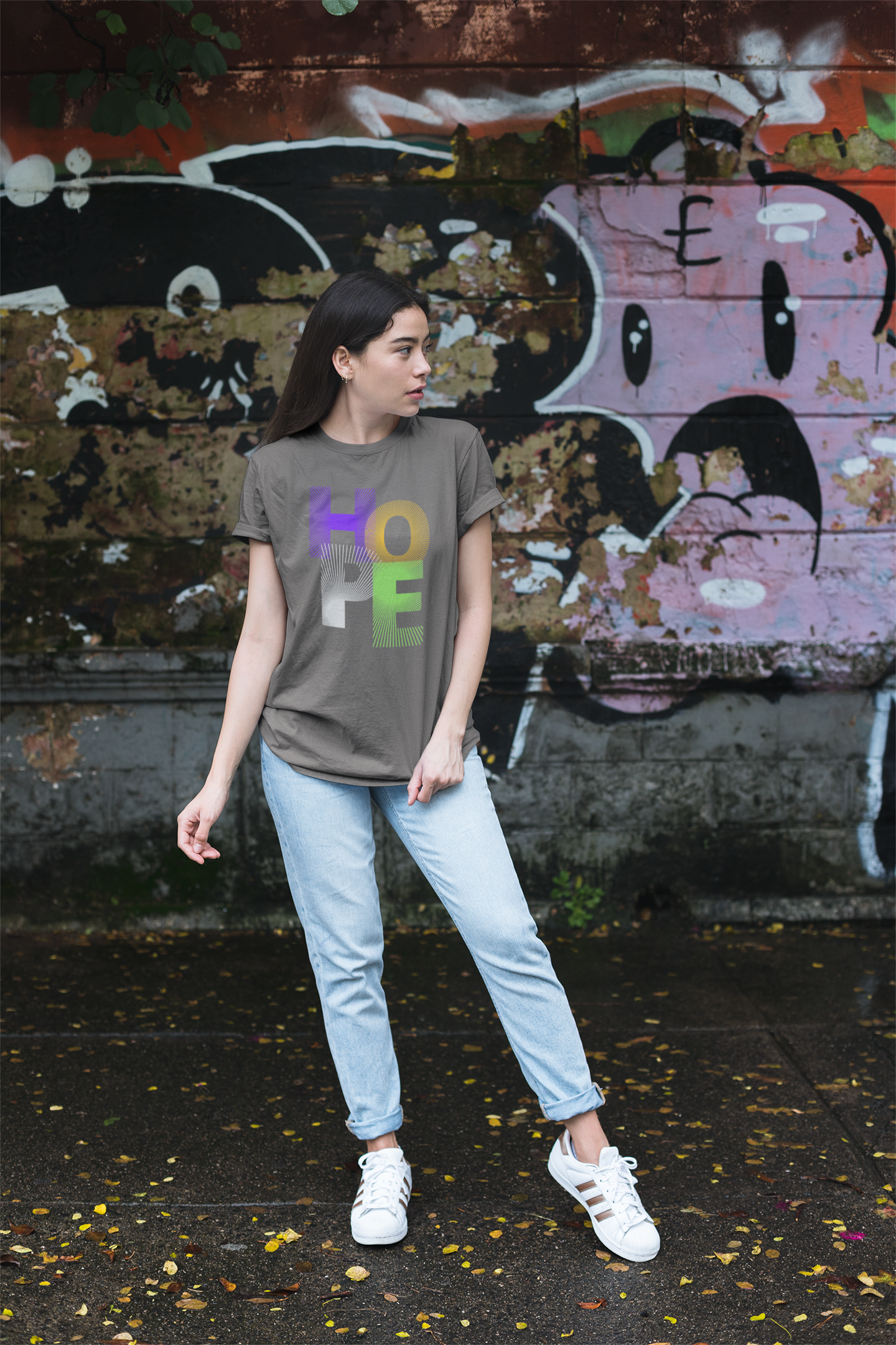 Person wearing a t-shirt with colorful letters standing in front of a graffiti-covered wall.