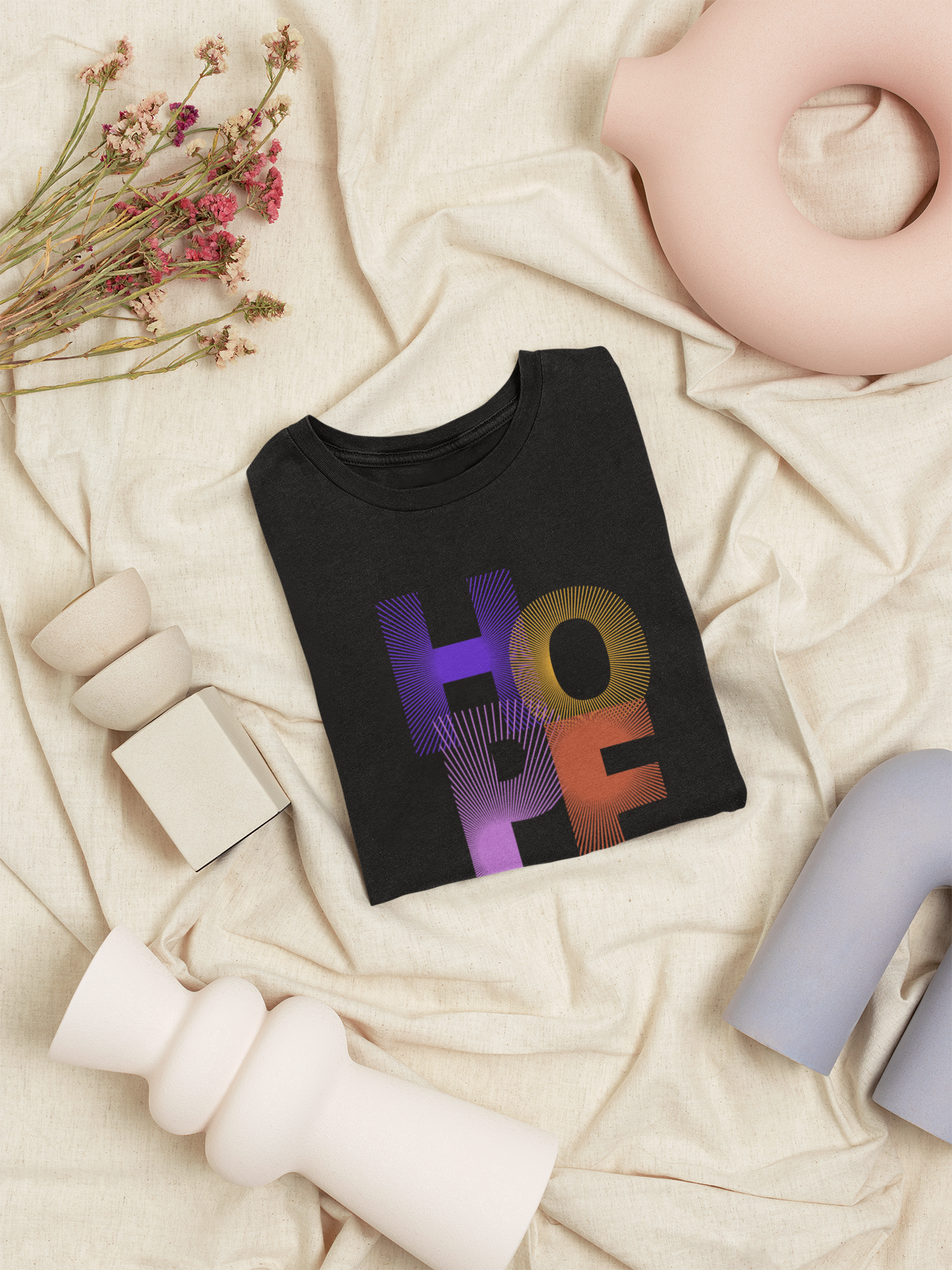 Black t-shirt with 'HOPE' in colorful letters on a beige surface with decorative elements.