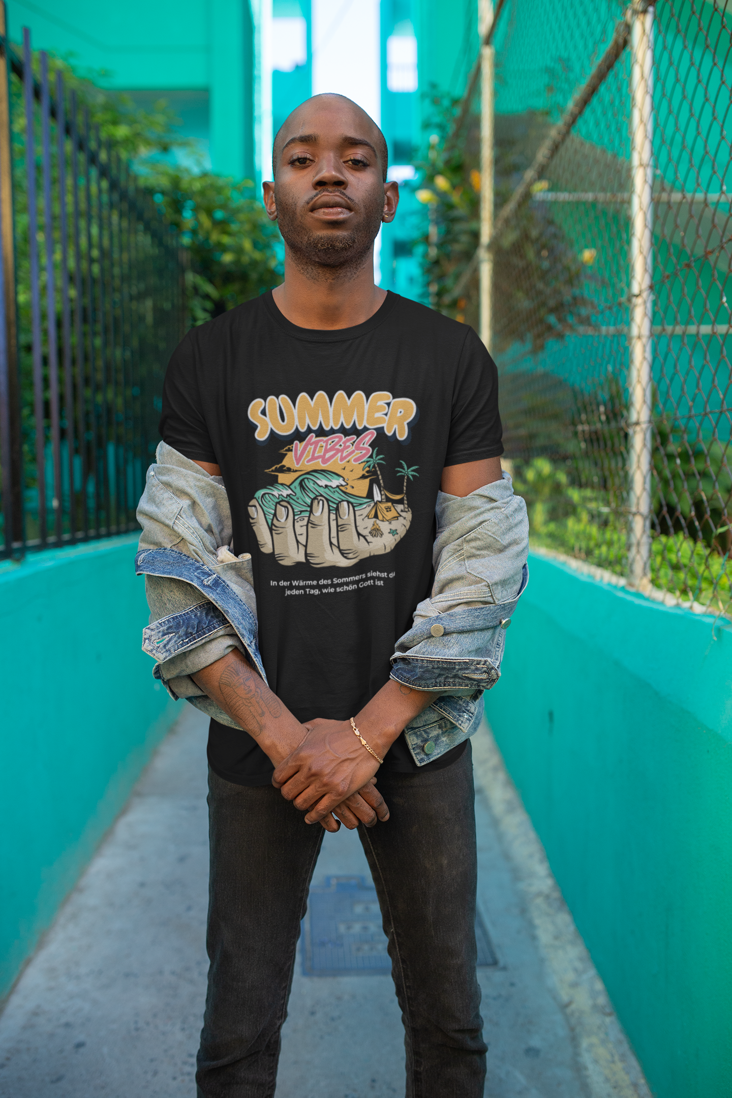 Person wearing a black t-shirt with colorful graphics and text, standing against a teal wall.